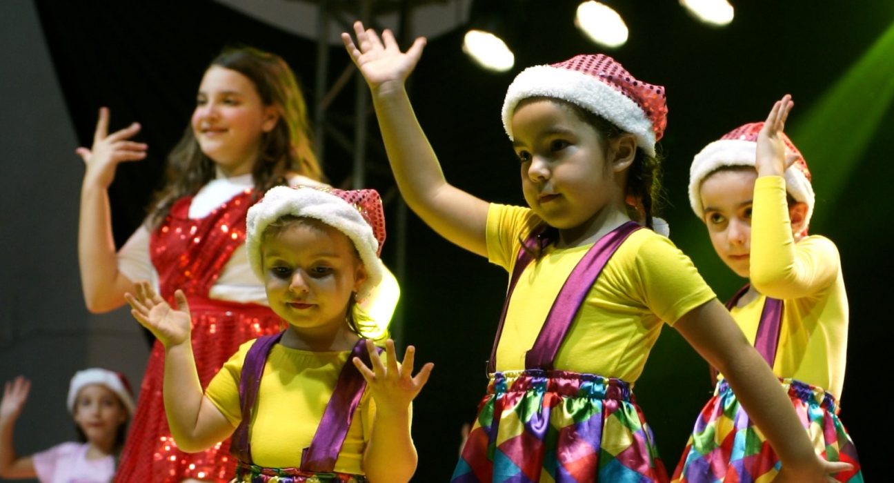 Grupos de dança se apresentam em palco decorado para o Natal.